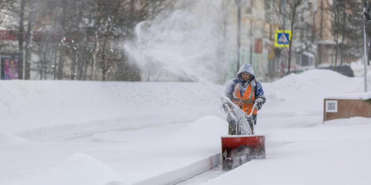 A man using a snowblower to clear snow from a driveway in Winnipeg during winter.